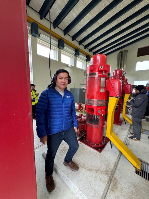 Elbek Ochilov standing inside a pumping station with red and yellow equipment