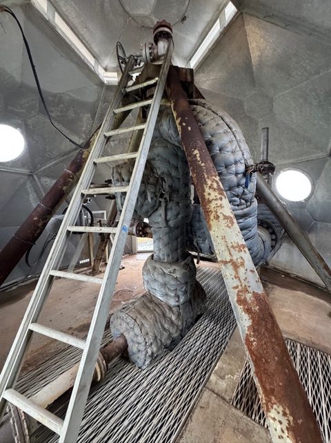 A steel wellhead with a ladder inside a well house