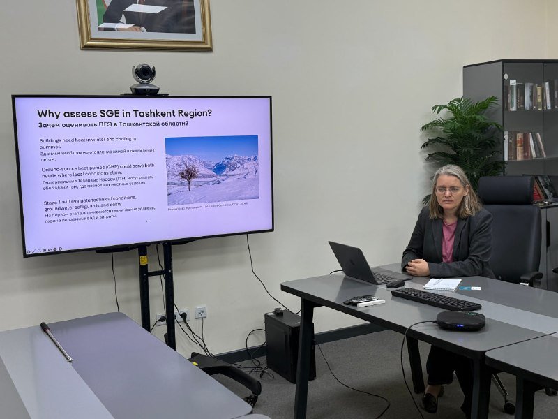 Женщина за ноутбуком рядом с экраном, на котором слайд «Why assess SGE in Tashkent Region?» на английском и русском языках