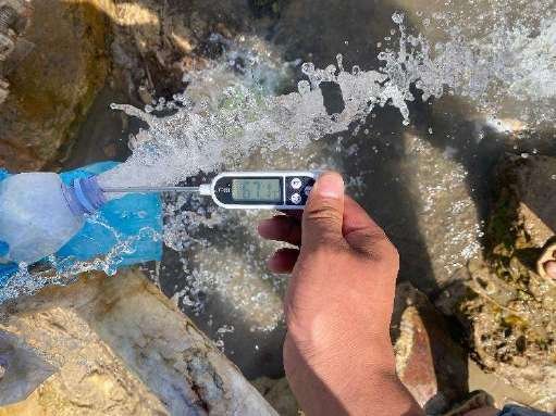 A hand holding a digital thermometer in water gushing from a geothermal source