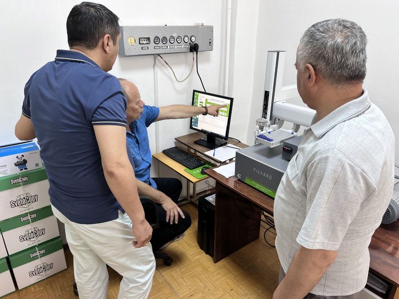 Picarro analizatori atrofida uch kishi; o‘tirgan kishi kompyuter ekraniga ishora qilmoqda