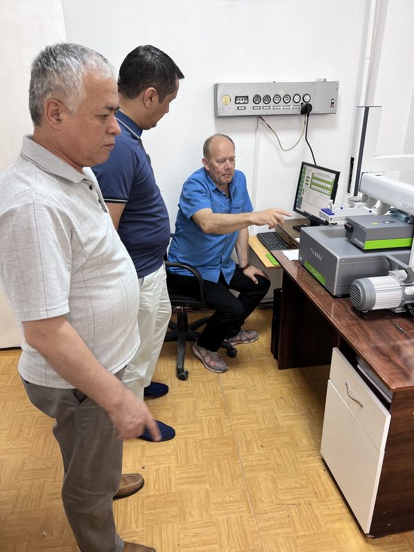 Picarro analizatori yonida ikki kishi turibdi, o‘tirgan hamkasbi kompyuterda ishlamoqda